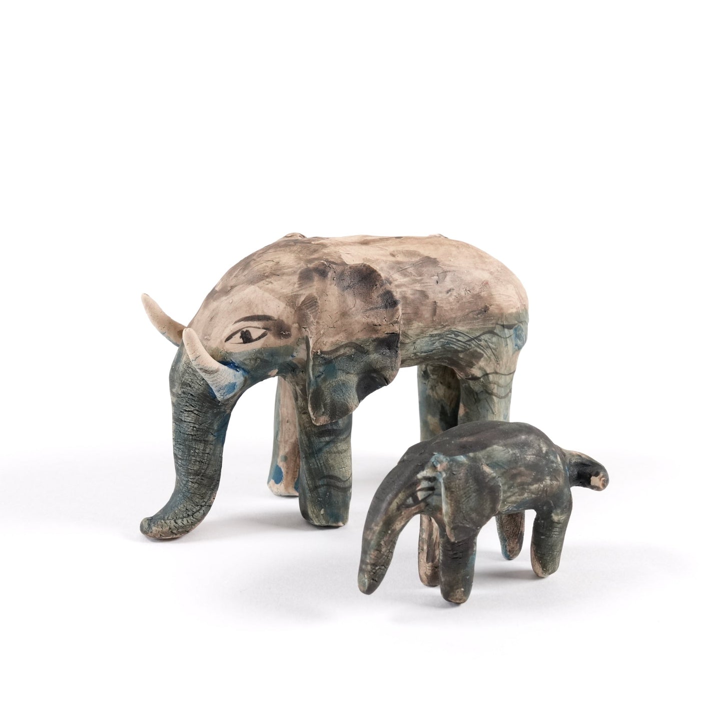 A painted ceramic elephant whistle with a ceramic painted calf. Both are in shades of beige, grey and blue and are standing on a plain white background.