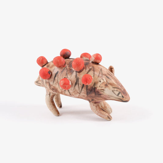 A painted ceramic hedgehog whistle in shades of brown with spherical red quills on a plain white background.