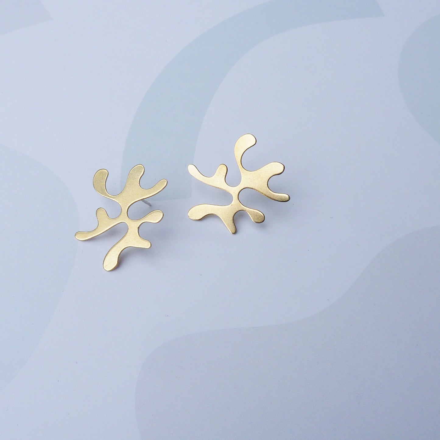 Gold abstract earrings on a light blue background