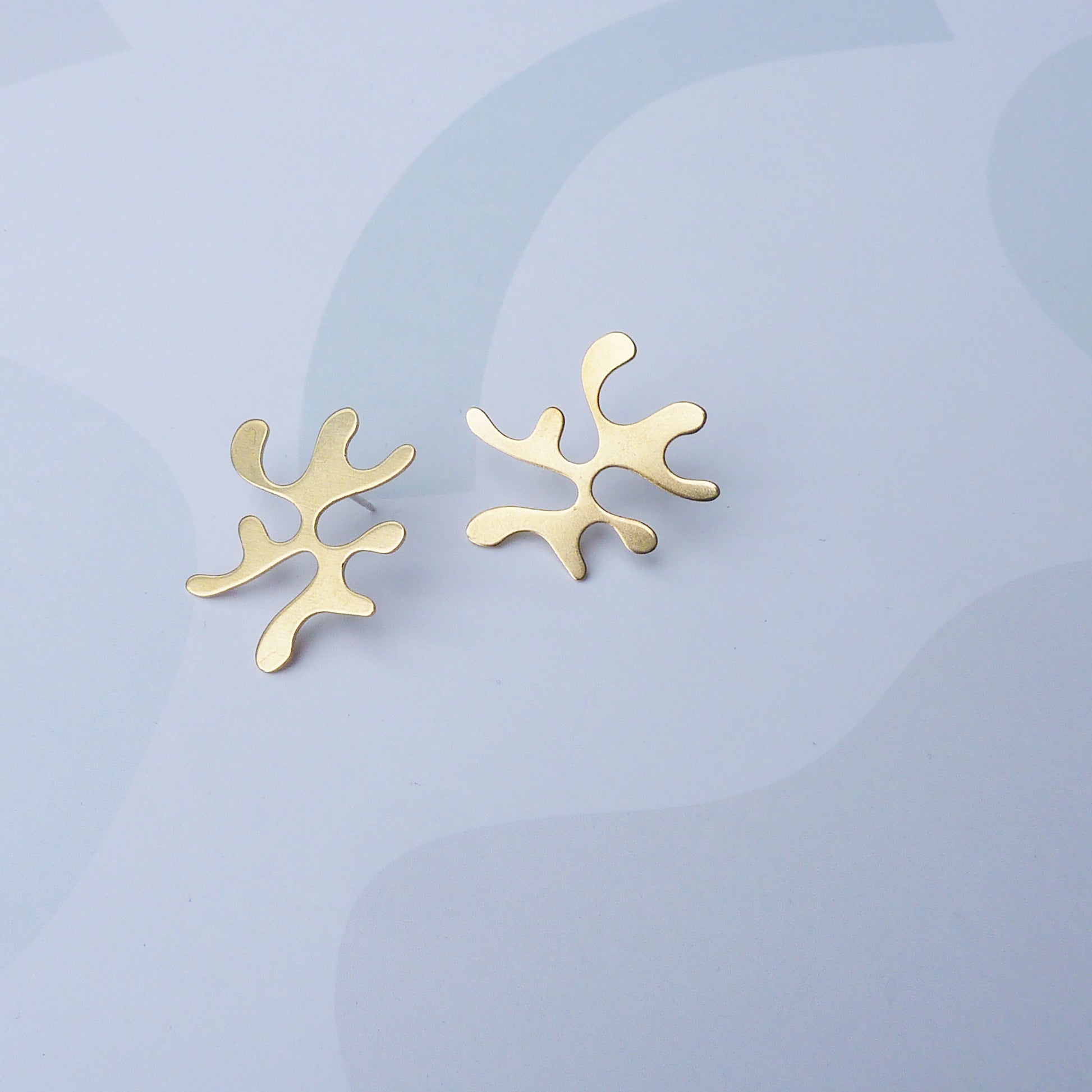 Gold abstract earrings on a light blue background