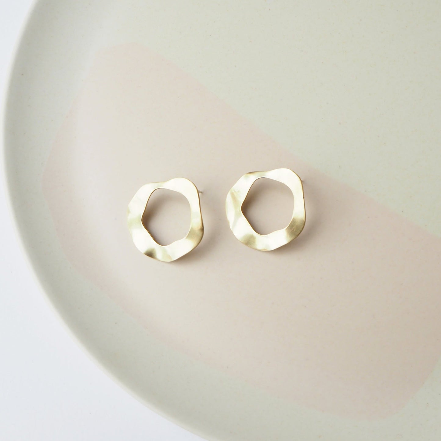 Gold hoop earrings on a light pink plate