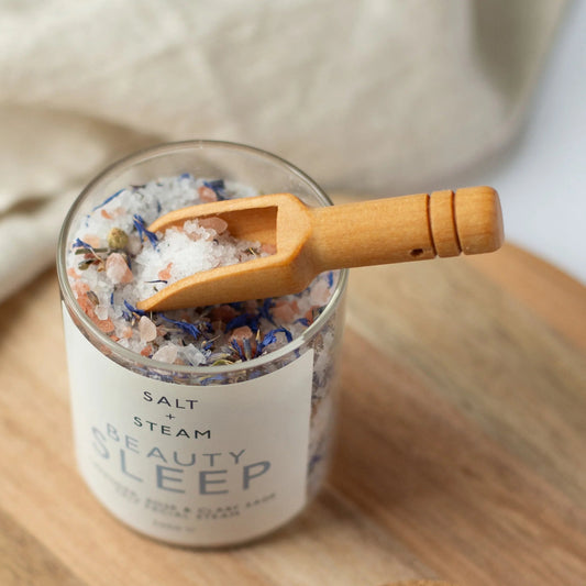 Jar of bath salts with a wooden scoop on a wooden board