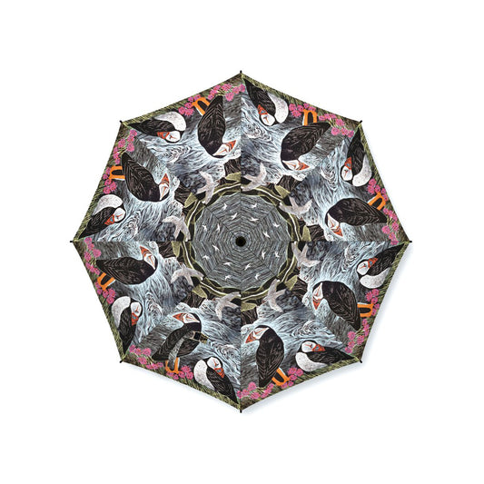 An open umbrella photographed from above on a plain white background, featuring a repeating kaleidoscopic print of puffins in black, white, gray, pink, and orange tones.