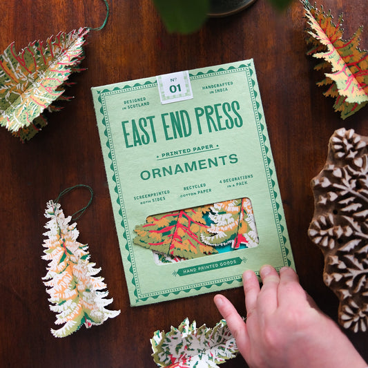 East End Press forest ornaments packaging on a wooden surface with decorative paper ornaments.