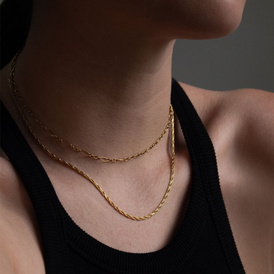 Close-up of a person wearing two layered gold necklaces against a dark background