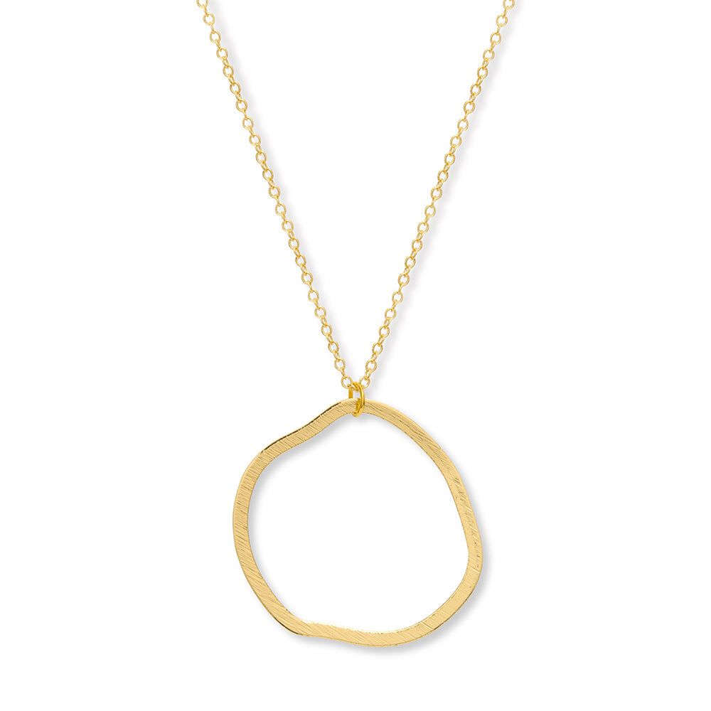 A close up of a gold chain and round gold circle pendant, the circle isn't perfectly round and has an abstract feel to it.