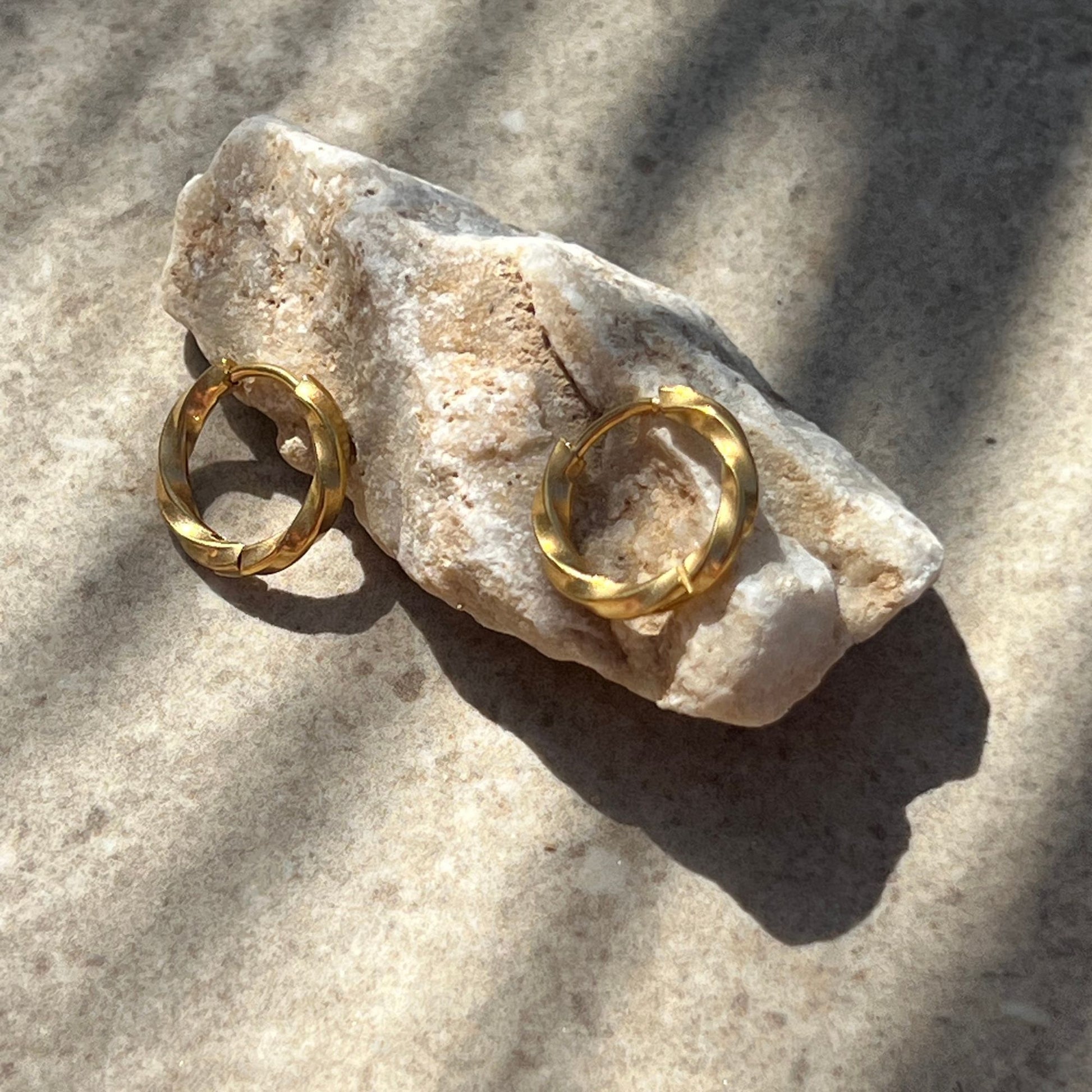 Twisted gold hoop earrings on a stone surface