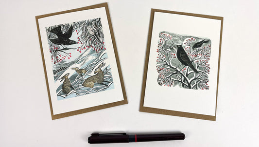 Two artistic greeting cards with nature-themed designs on a white surface with a pen.