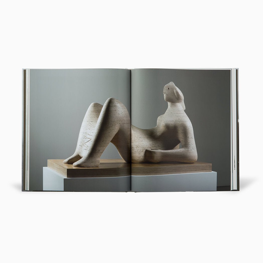 Open book with a full bleed image spread featuring stone sculpture of a seated figure on a wooden base.