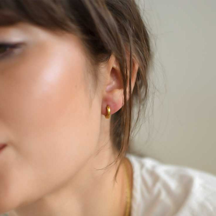A close-up image of a person wearing a pair of small gold hoop earrings.