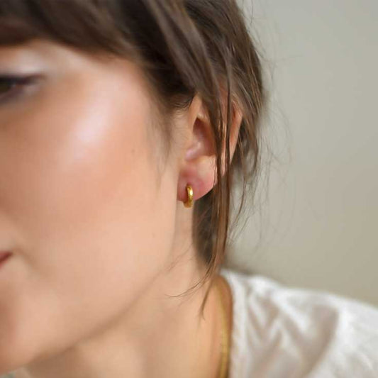 A close-up image of a person wearing a pair of small gold hoop earrings.