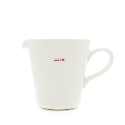 A white porcelain jug with the word 'love' written on it in red, having a pouring spout and handle.