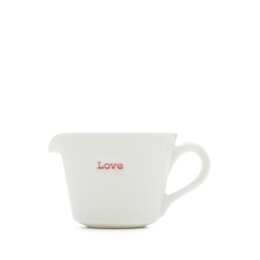 A white porcelain jug with the word 'love' written on it in red, having a pouring spout and handle.
