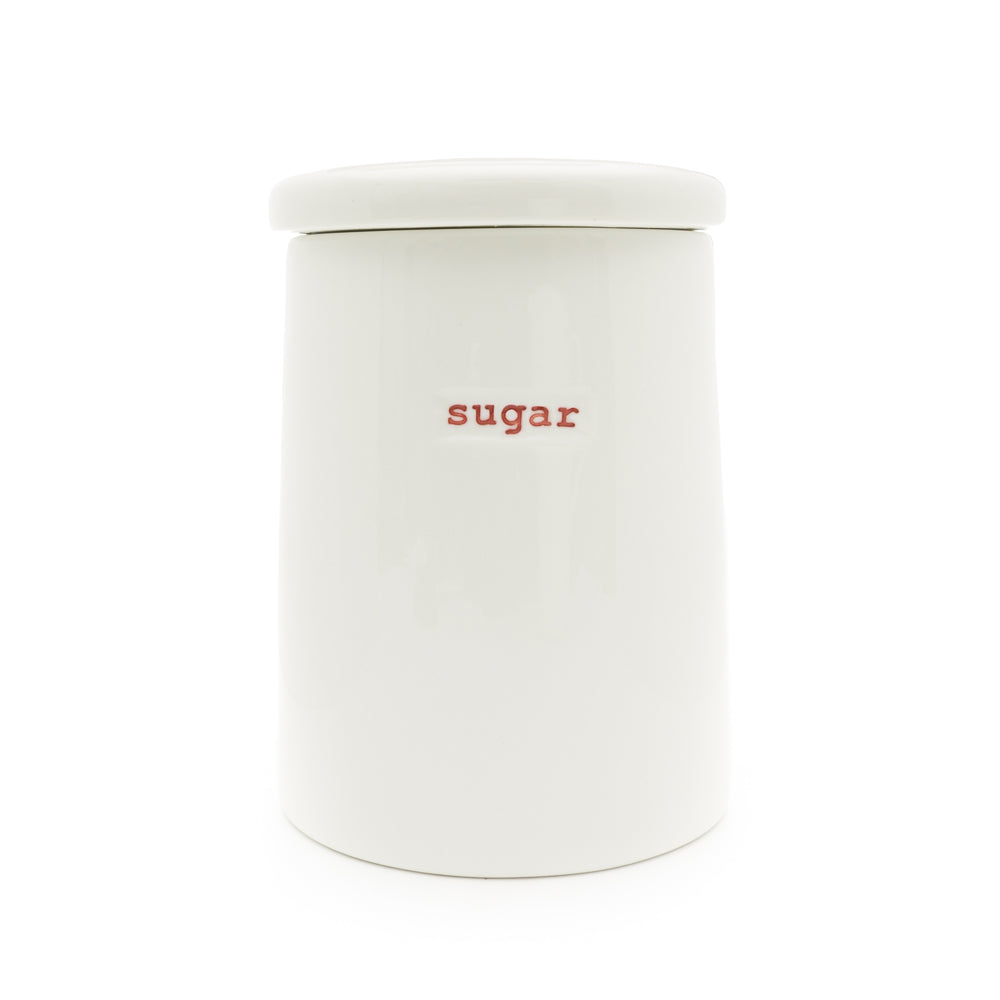 A white porcelain storage jar with the word 'sugar' written on it in red, having a lid.