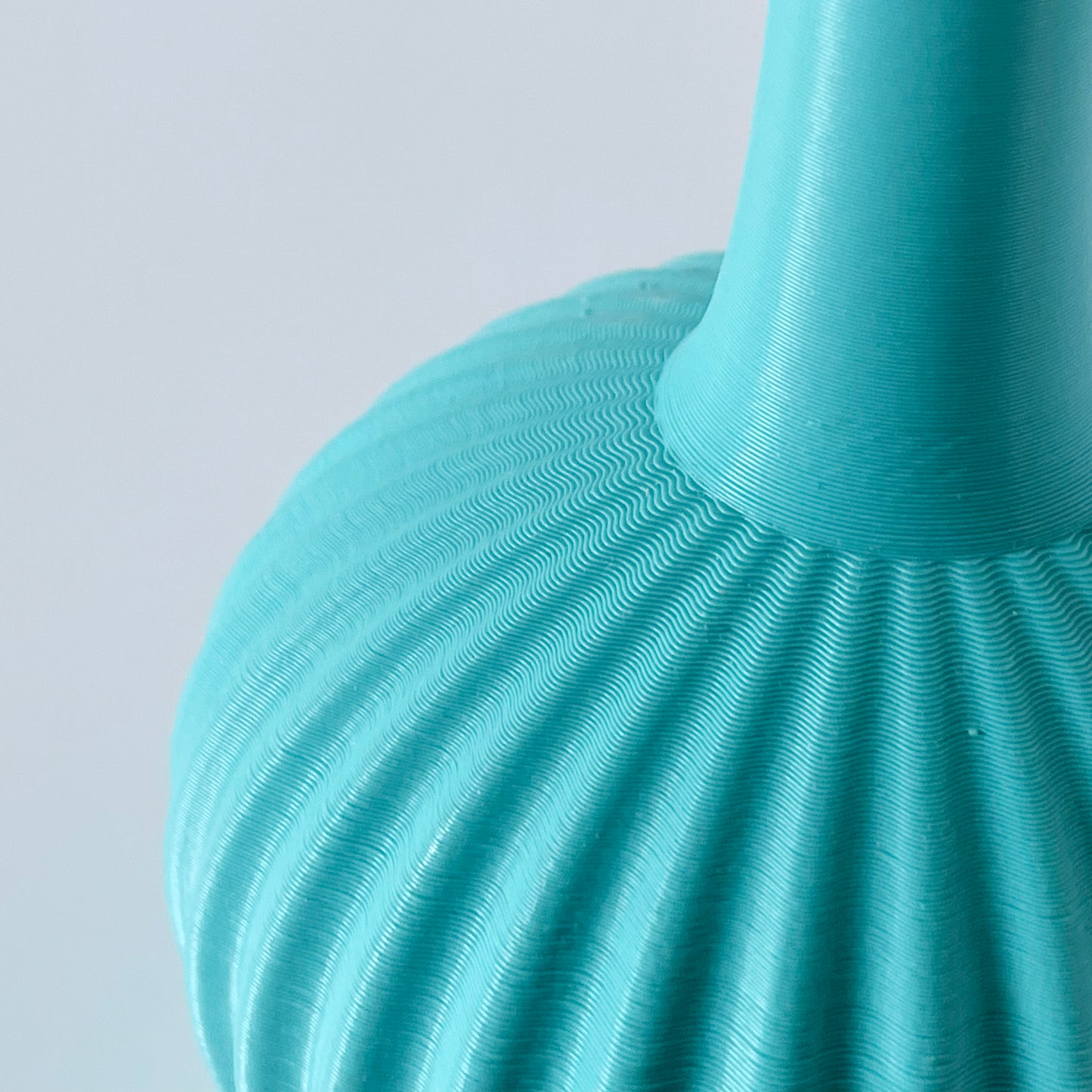 A close up showing the wavy ribbed texture of a 3D printed turquoise vase.