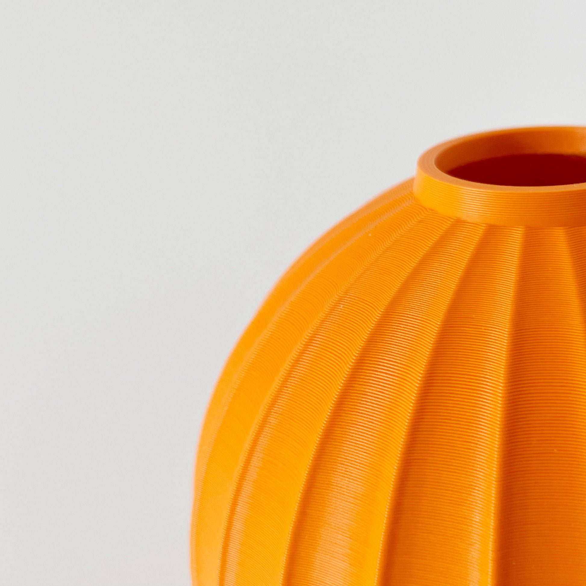 The outside of a spherical 3D printed orange vase with ribbed textures.