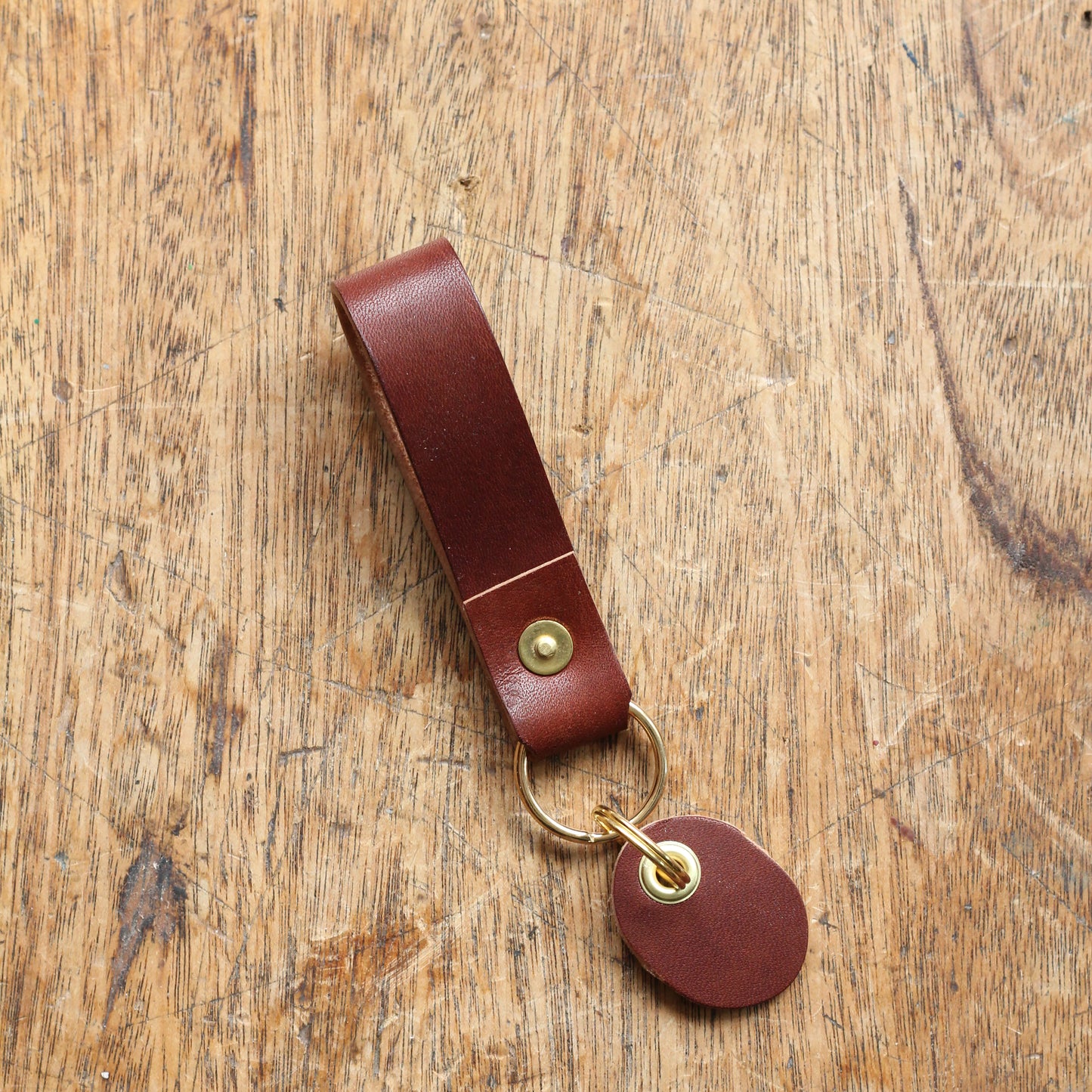 A brown leather key fob with a brass ring and a brass tag, placed on a wooden surface.