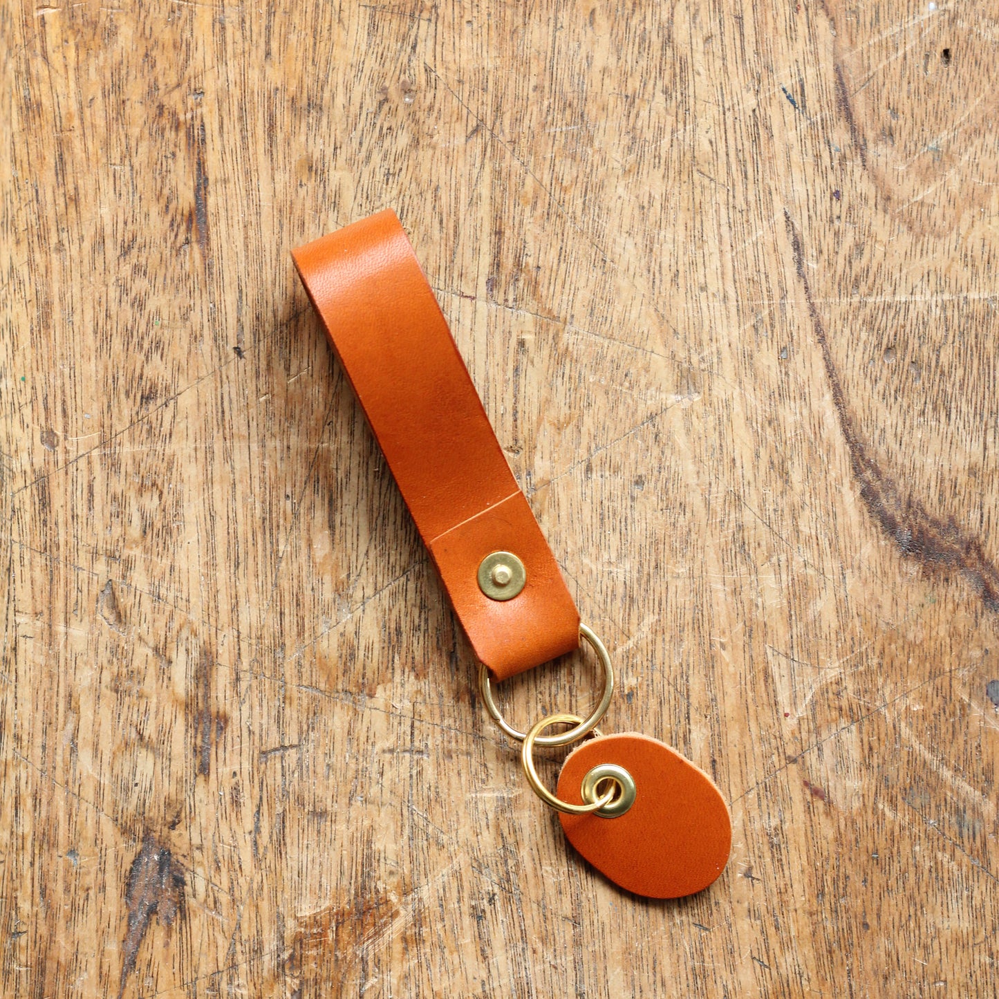 A tan leather key fob with a brass ring and a brass tag, placed on a wooden surface.