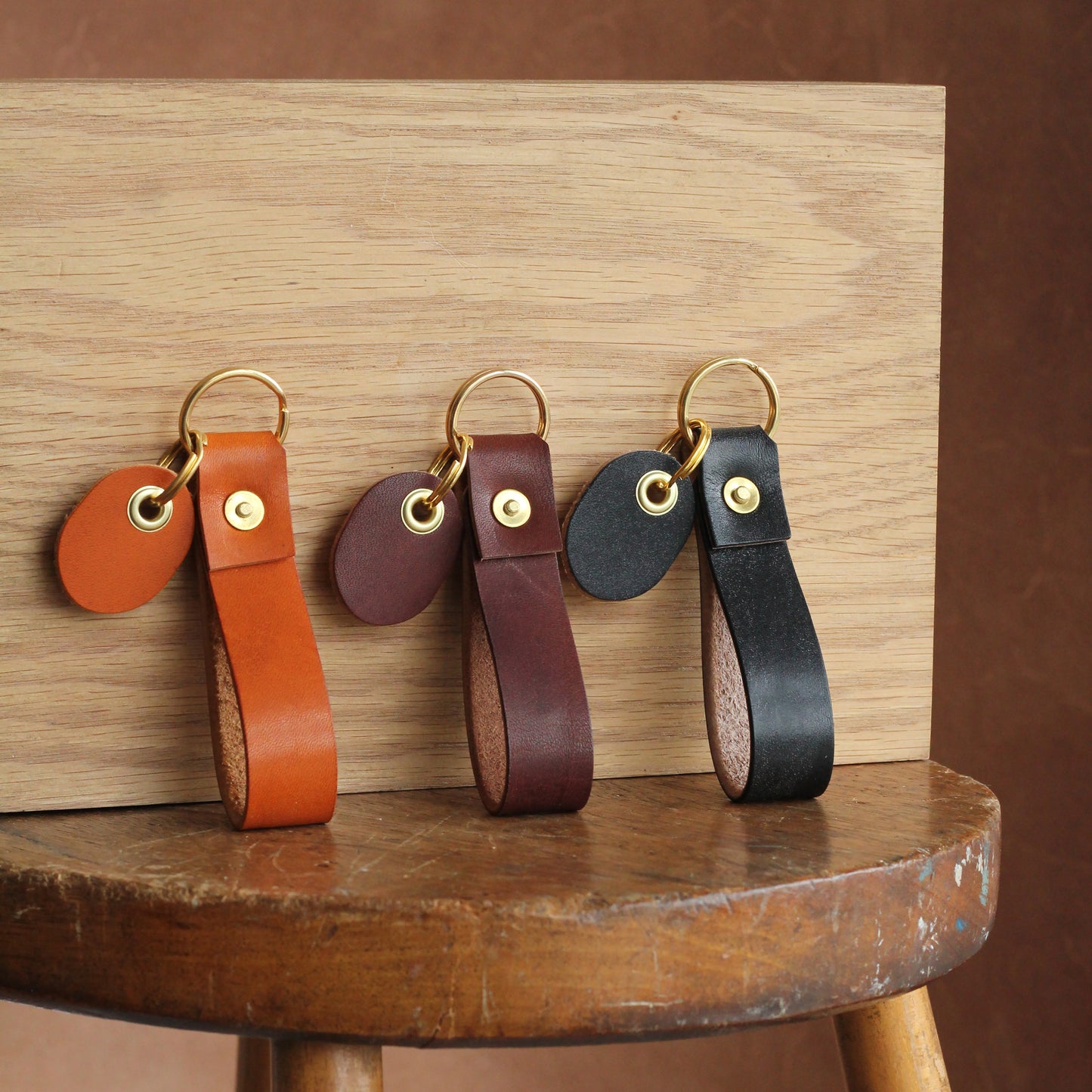 Three leather key fobs standing up on a table next to each other, featuring brass rivets and a leather tag.