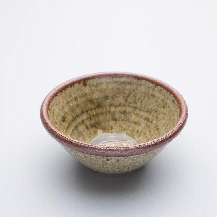 A small stoneware ceramic bowl with a beige and greenish hue and a dark brown rim.