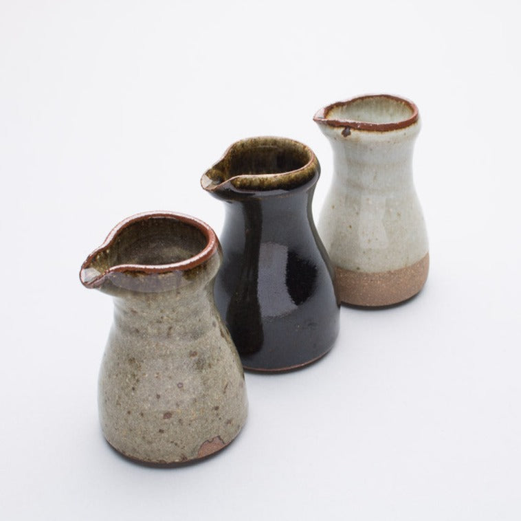 A row of three ceramic pourers, reduction fired, from Leach Pottery.