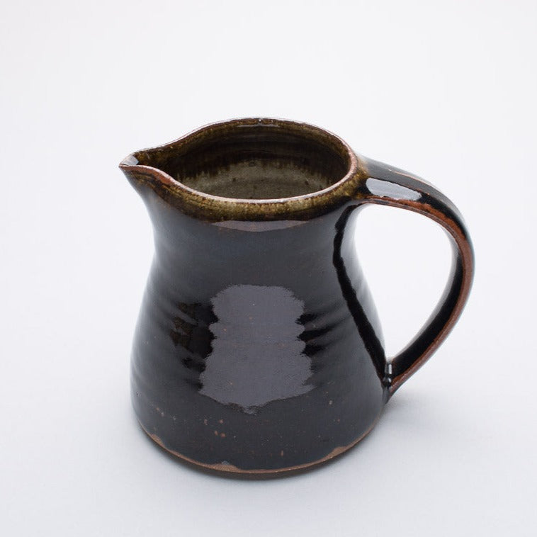 A small ceramic jug with a two-tone colour, primarily a brownish hue with a darker brown at the rim and handle.