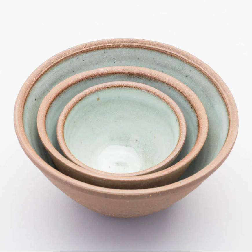 Set of three ceramic bowls stacked inside of each other with a green colour on the inside and a brown outer on a white background