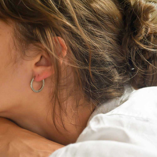 A close-up image of a person's ear wearing a larger silver hoop earring.