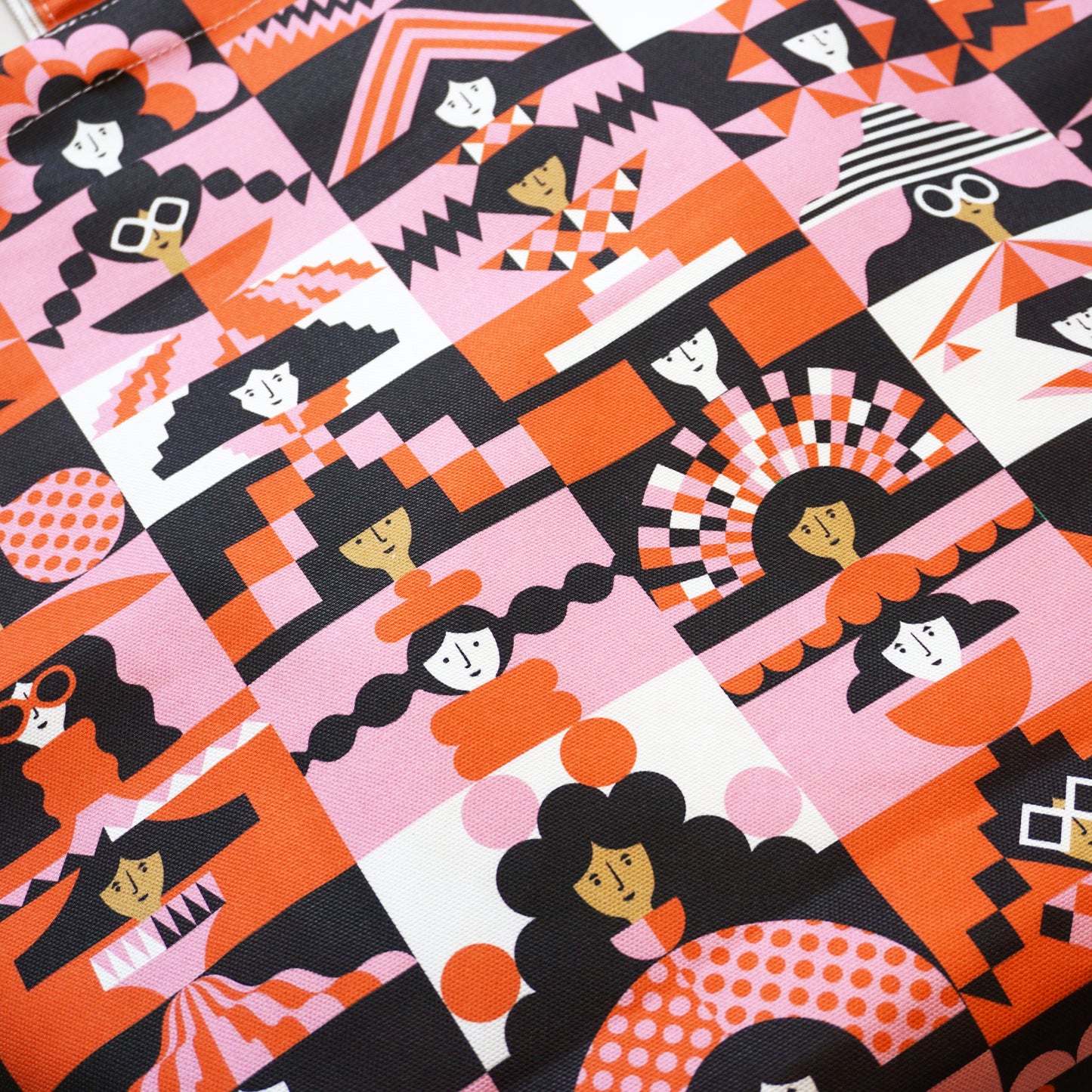 Patterned close up of fabric with stylised, geometric figures in black, pink, and orange.