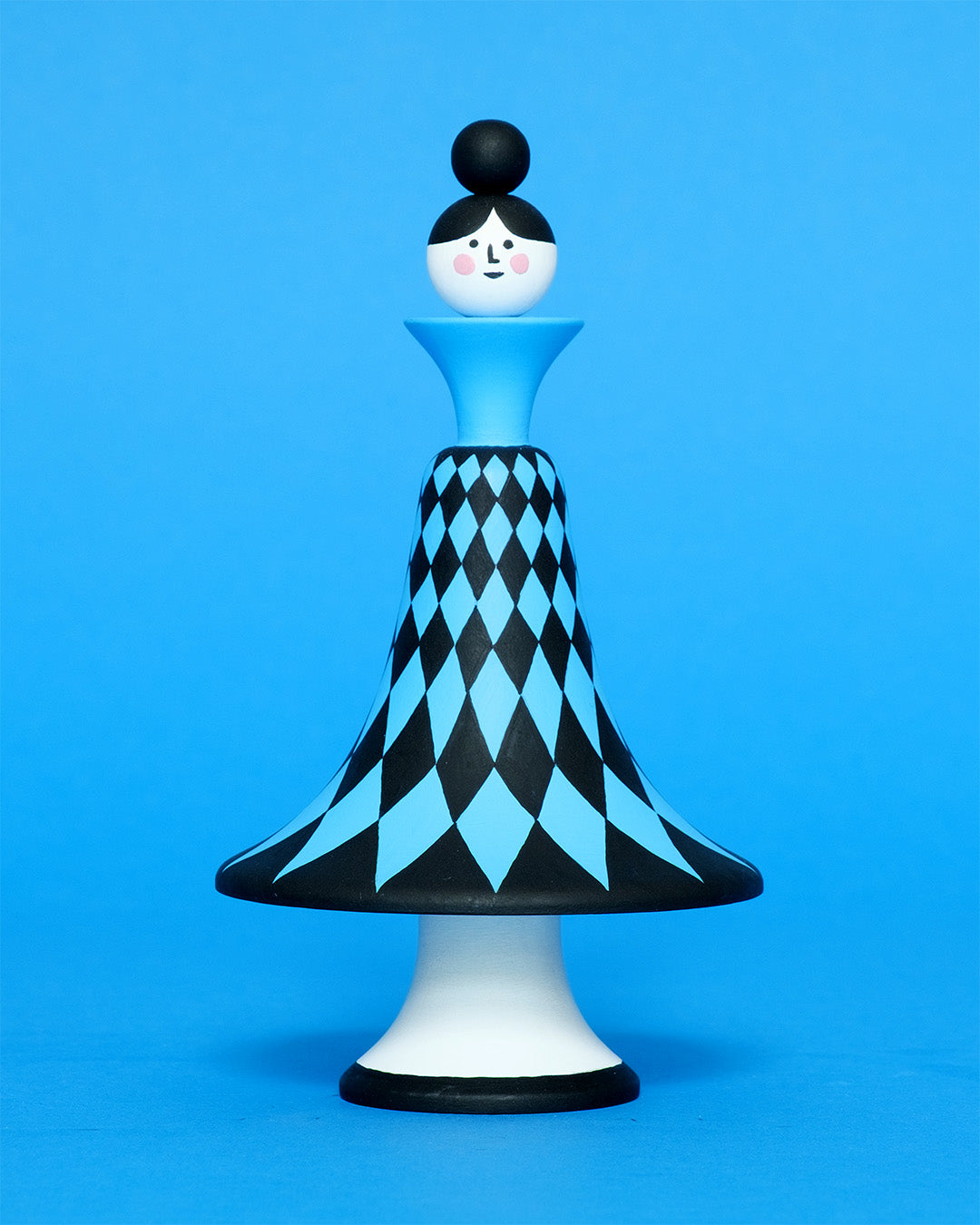 A colourful sculpture with a black and blue diamond patterned curved body with white legs on a plain blue background.