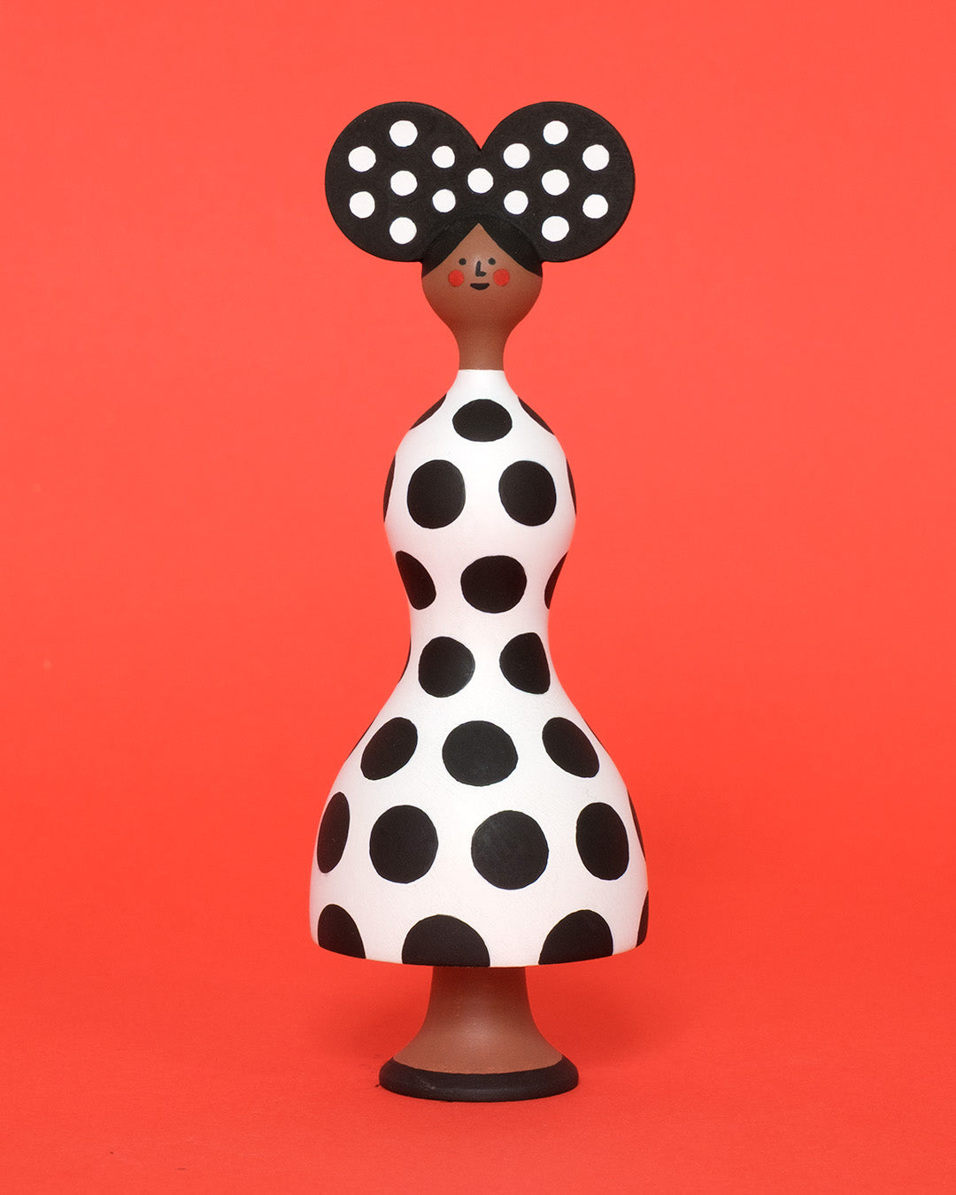 A monochrome sculpture with a black and white spotty body with a matching headdress on a plain white background.