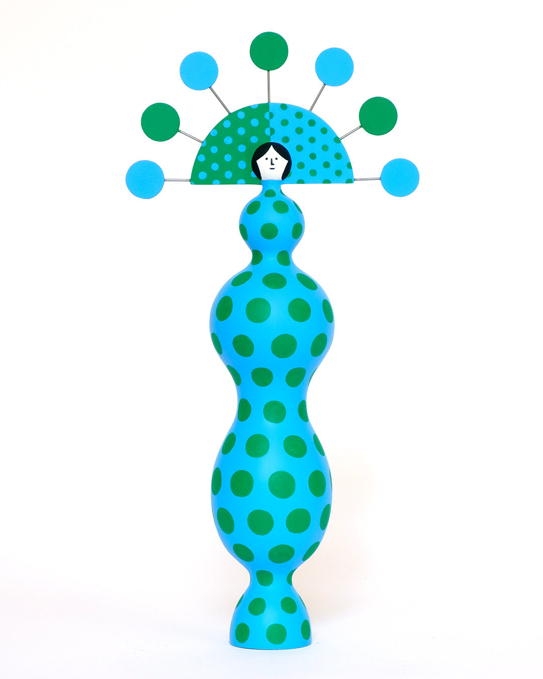 A colourful sculpture with a blue and green spotty body with a matching headdress on a plain white background.