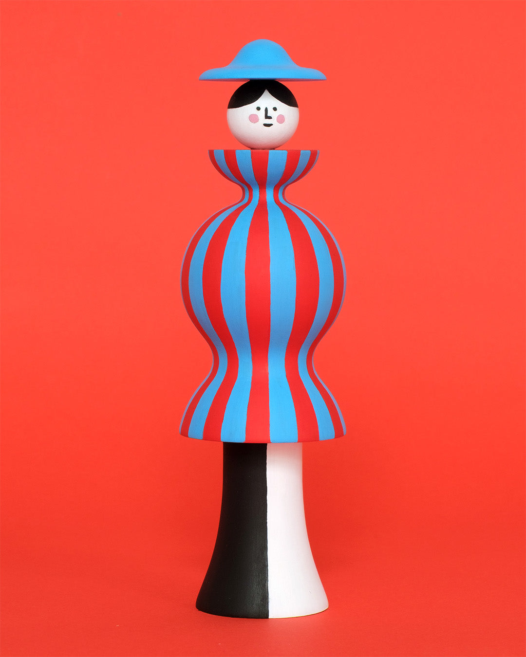 Colourful sculpture of a figure made from a red and blue stripey body with white and black legs with a blue hat on a plain orange background.