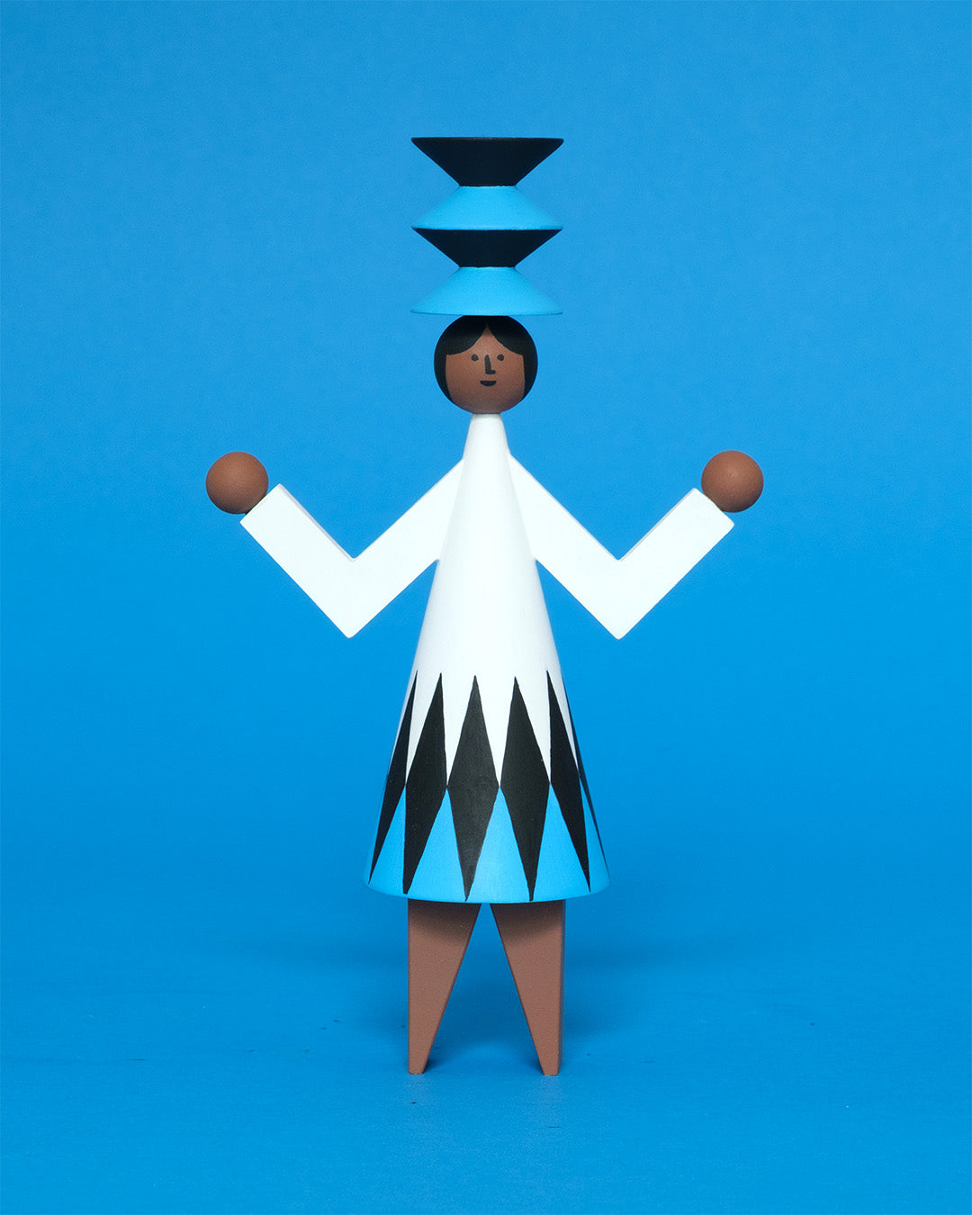 A colourful wooden sculpture with a black, white and blue diamond patterned dress with brown legs and a matching blue and black headdress on a plain blue background.