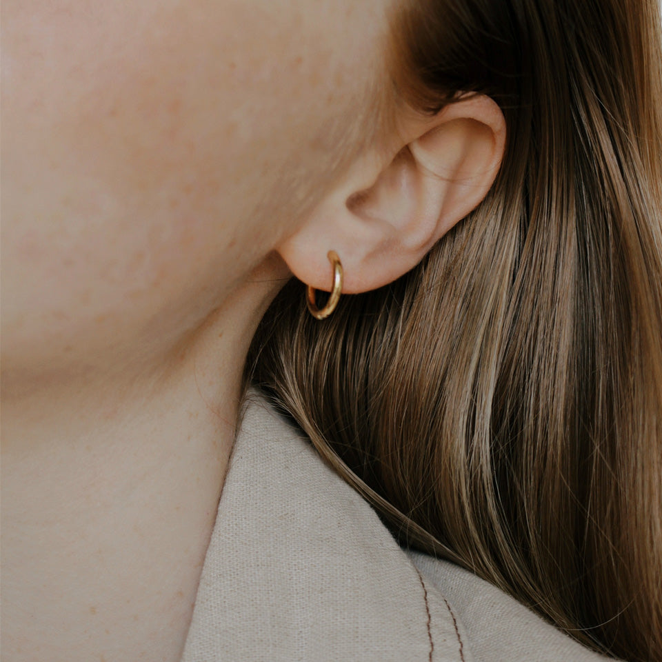 A close-up image of a person's ear wearing a gold-colored hoop earring.