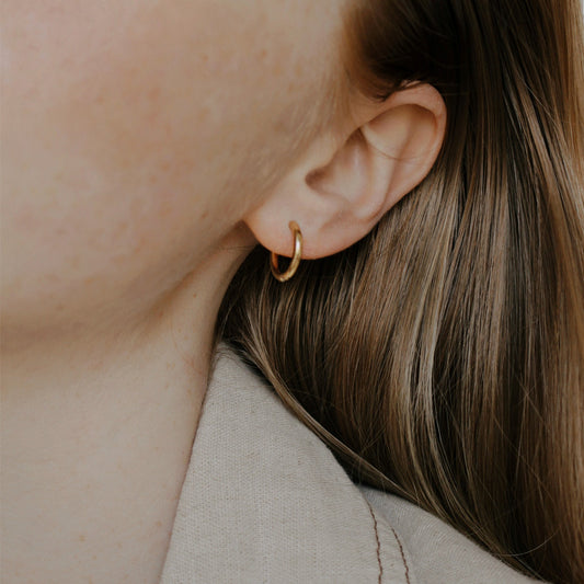 A close-up image of a person's ear wearing a gold-colored hoop earring.