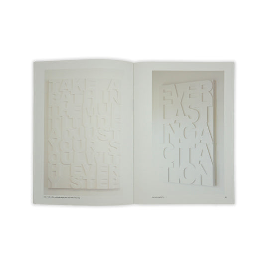 An open spread showing an image of a white stone carving with letters carved in on both pages with very minimal text.