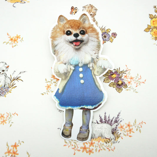 A die-cut postcard of a dog with a fluffy head and a human-like body, dressed in a blue dress with white buttons. The background features floral patterns and small animal illustrations, creating a playful and imaginative scene.
