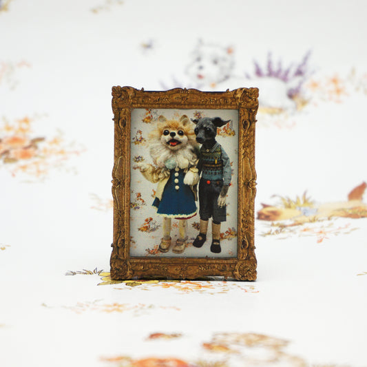 A small, ornate gold frame holds a whimsical illustration of two anthropomorphic animals dressed in vintage clothing. The background features a soft, floral pattern, adding a charming, nostalgic feel to the scene.