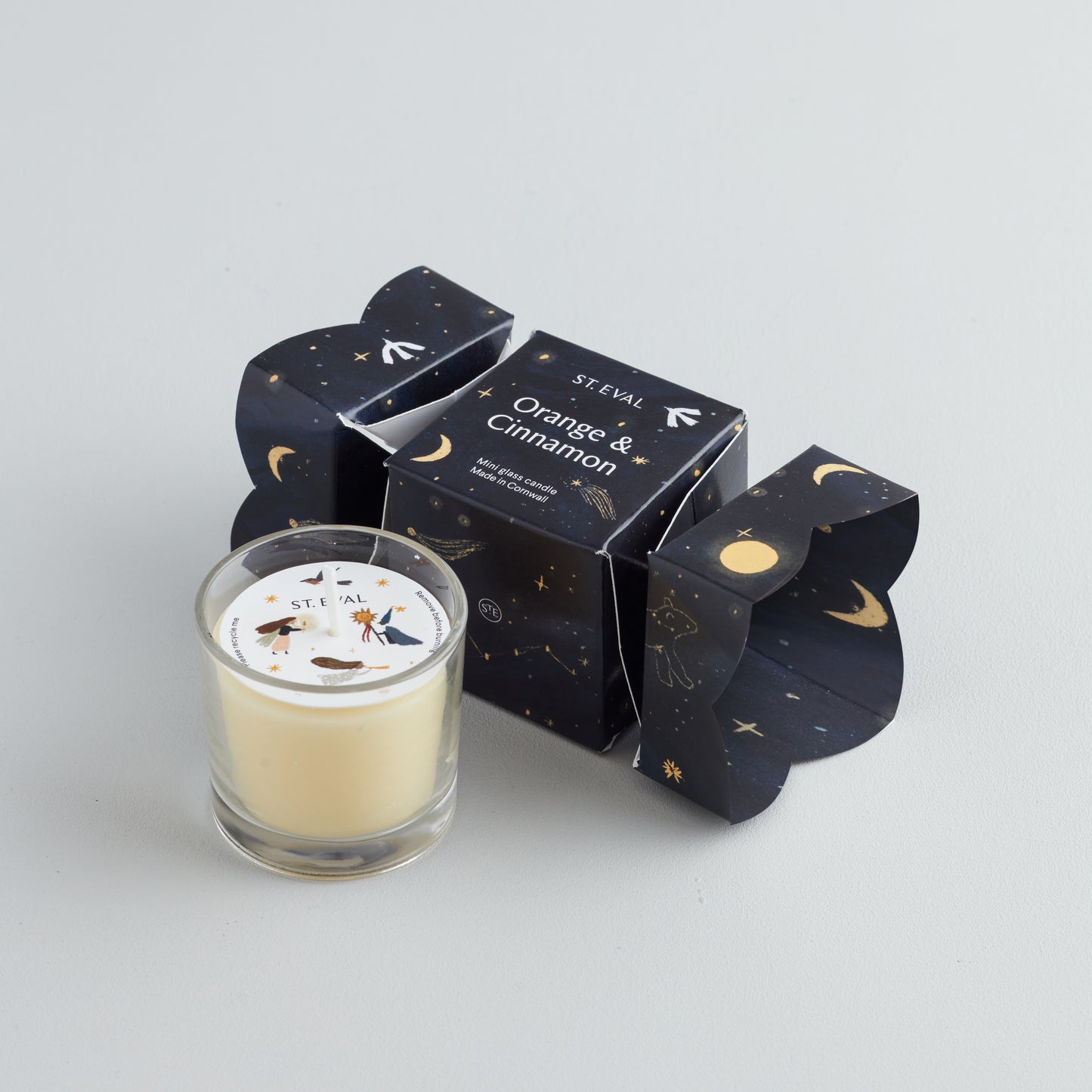 A small glass candle in a decorative box with 'St Eval' branding, featuring a stars and crescent moon design, and labelled 'ORANGE & CINNAMON'.