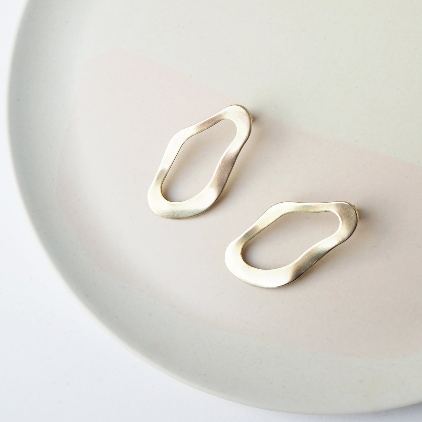 Wavy round gold stud earrings on a round beige stone