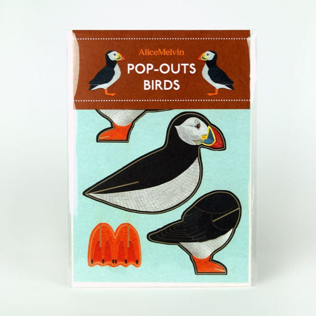 A colourful packaging featuring pop-out bird designs, specifically puffins. The top label reads "Alice Melvin Pop-Outs Birds." The background is light blue, and the puffins are illustrated with vibrant details and orange feet.