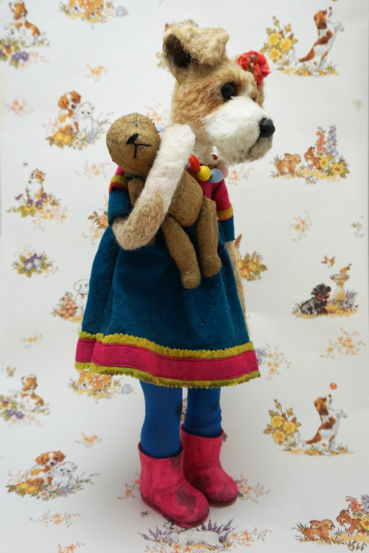 A plush dog dressed in a blue dress with pink trim, colourful bead necklace, and pink boots, holding a smaller plush bear. The background features a pattern of various playful animals and floral designs.