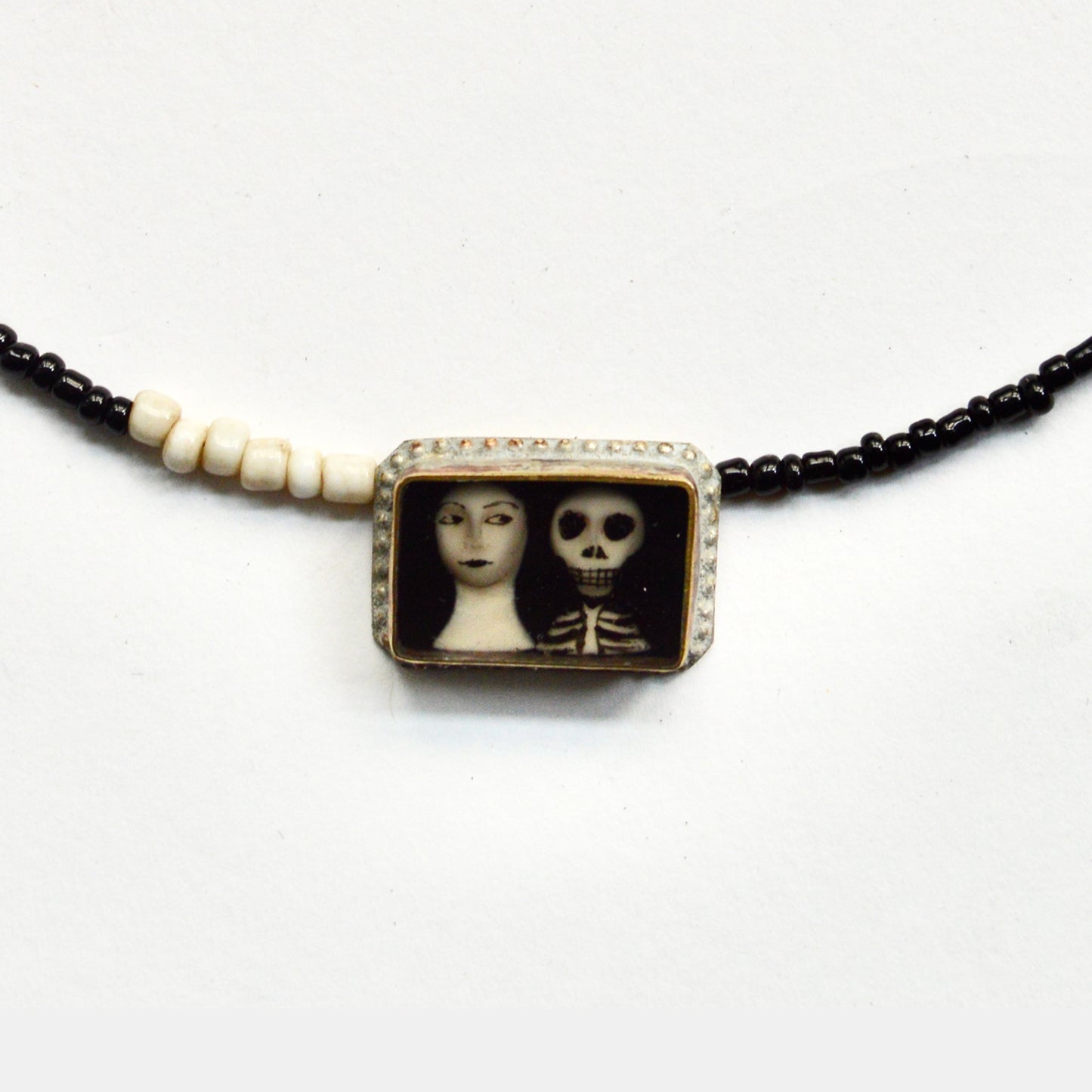 The pendant attached at the front shows an illustration of a women's neck and face next to a skeletons head and ribs.