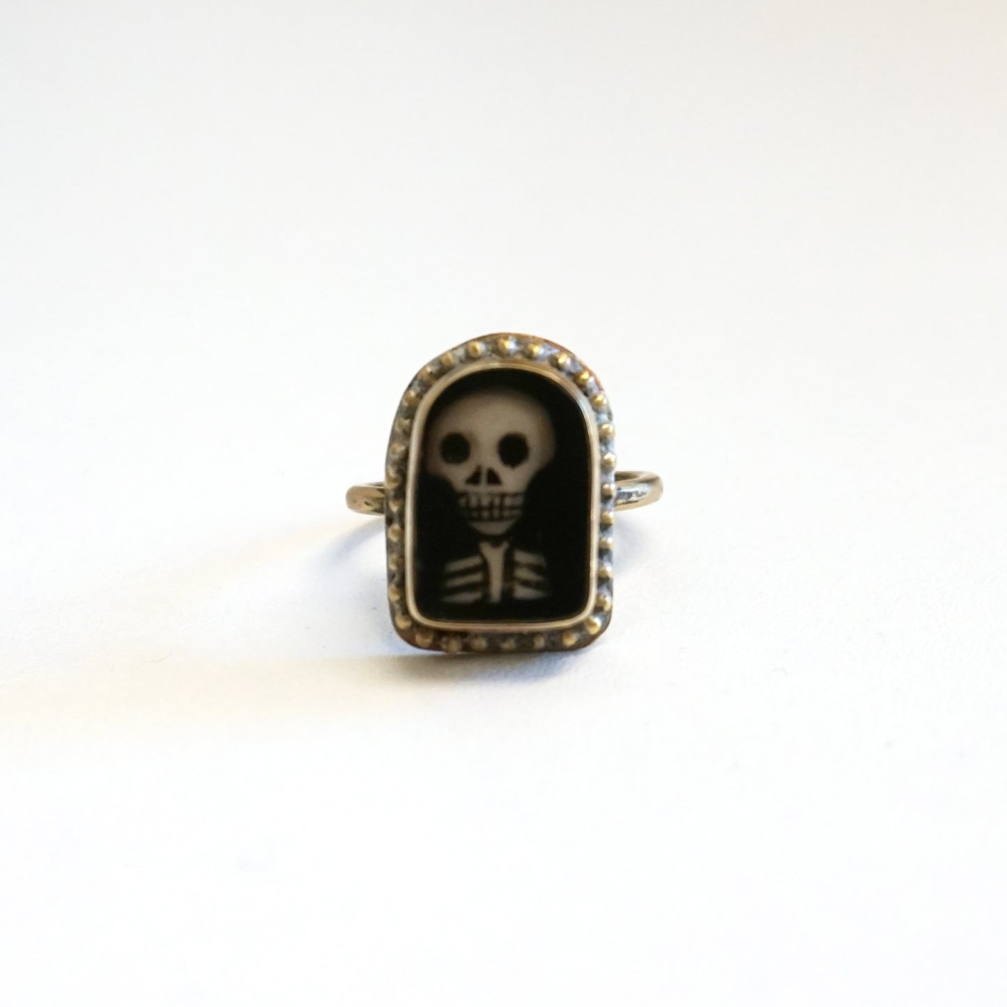 An arch shaped ring featuring a miniature portrait of a skeleton's head and shoulders.
