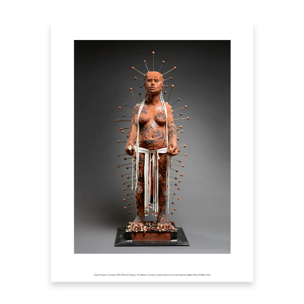 A life-sized sculpture of a figure covered in intricate body art and clay, standing confidently. The figure is adorned with numerous pins radiating from the head, and white ribbons hang from the waist, set against a dark background.