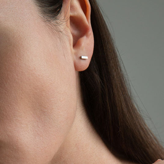 A close-up image of a person's ear wearing a silver bar stud earring.