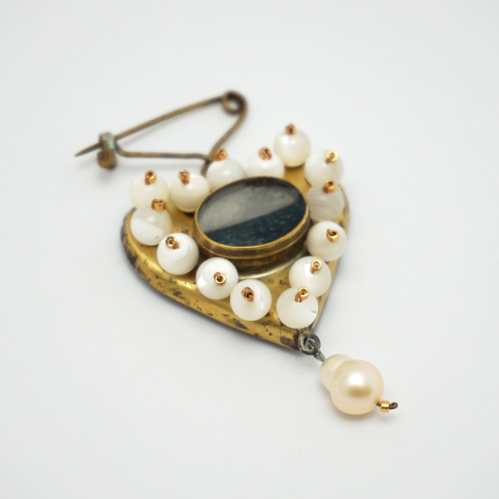 Gold coloured heart-shaped brooch with pearls on the outer edge and a central hand painted ocean insert. The brooch is on a plain white background and features a single pearl dangling from the bottom of the heart.