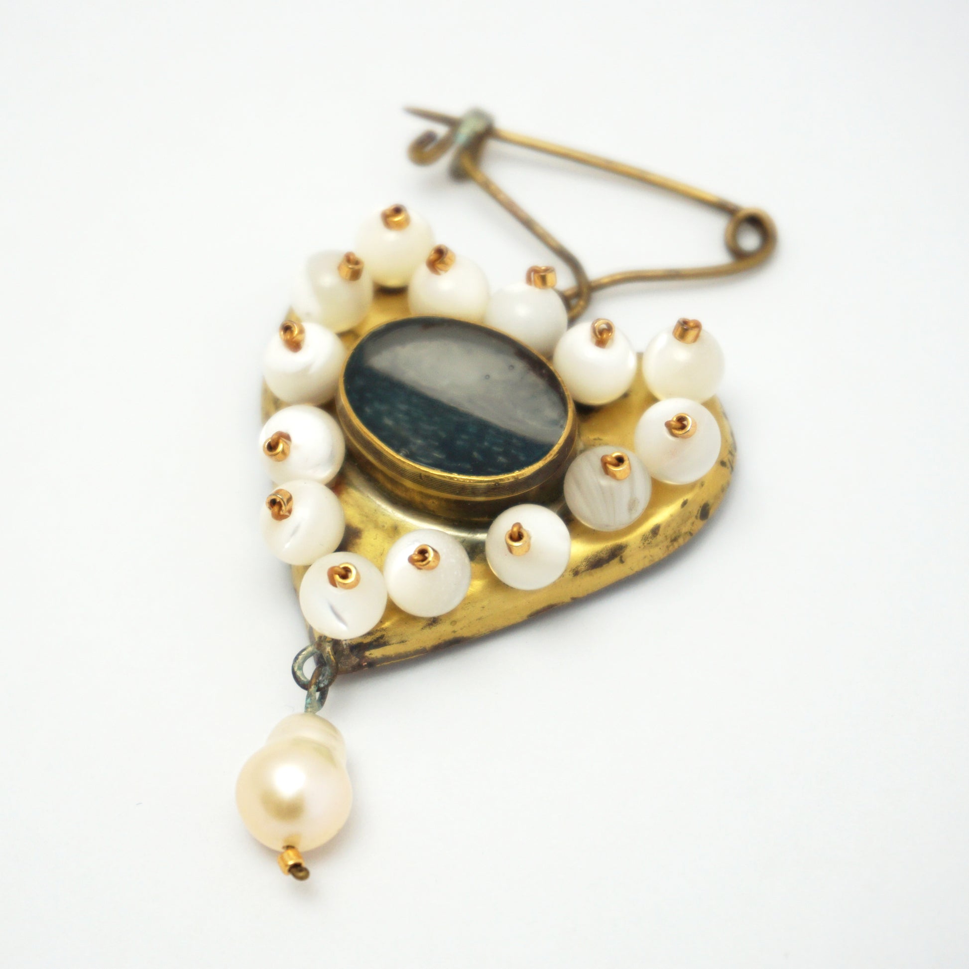 Gold coloured heart-shaped brooch with pearls on the outer edge and a central hand painted ocean insert. The brooch is on a plain white background and features a single pearl dangling from the bottom of the heart.