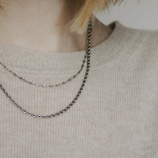One necklace that gives the appearance of two silver necklaces layered on a person wearing a beige jumper.
